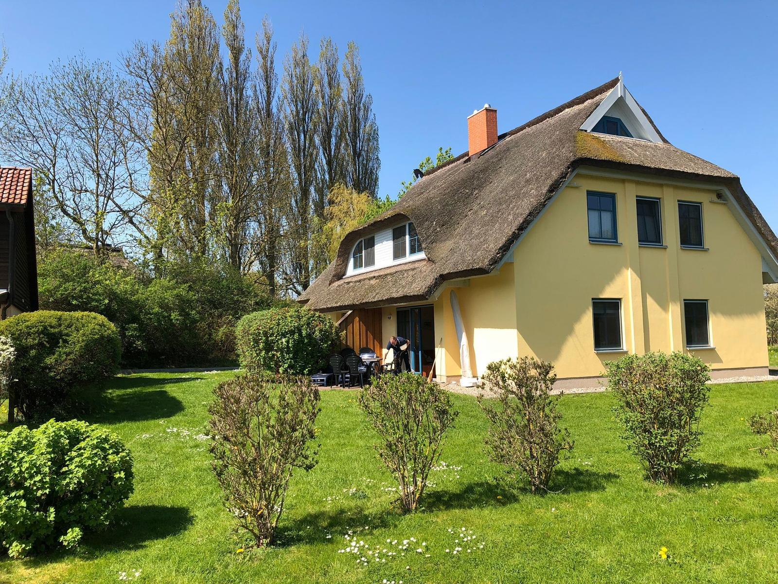Haus mit Strohdach und Garten. Terrasse mit Tisch und Stühlen.