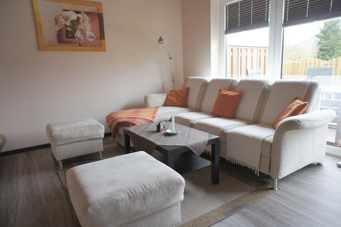 Wohnzimmer mit Sofa, Hocker und Tisch. Fenster mit Jalousie und Wandbild.