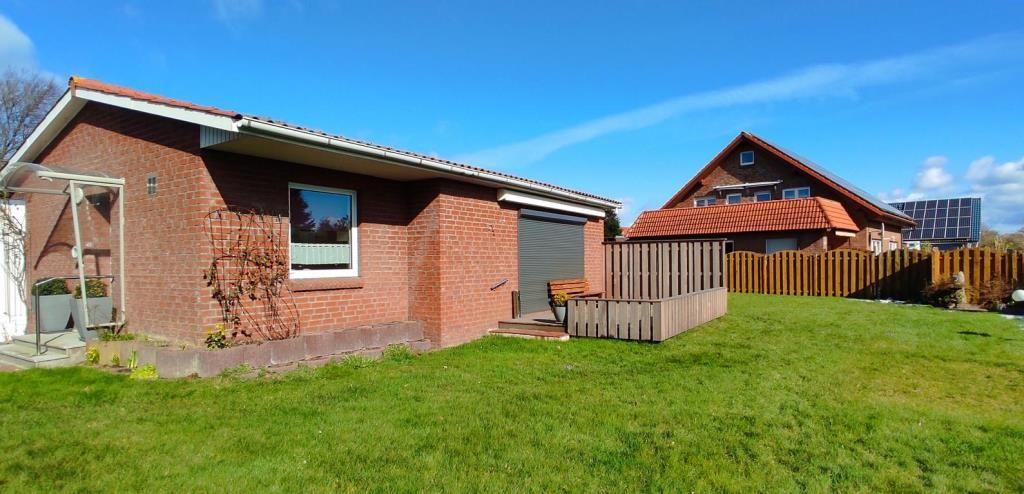 Rotes Backsteinhaus mit Garten und Terrasse. Im Hintergrund ein weiteres Haus mit Solaranlage.