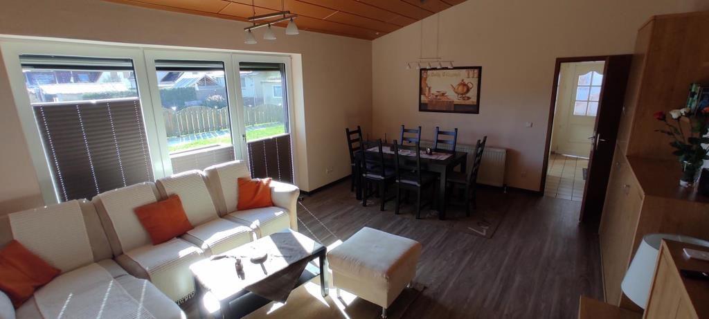 Wohn- und Essbereich mit Sofa, Tisch und Fenster zur Außenterrasse.