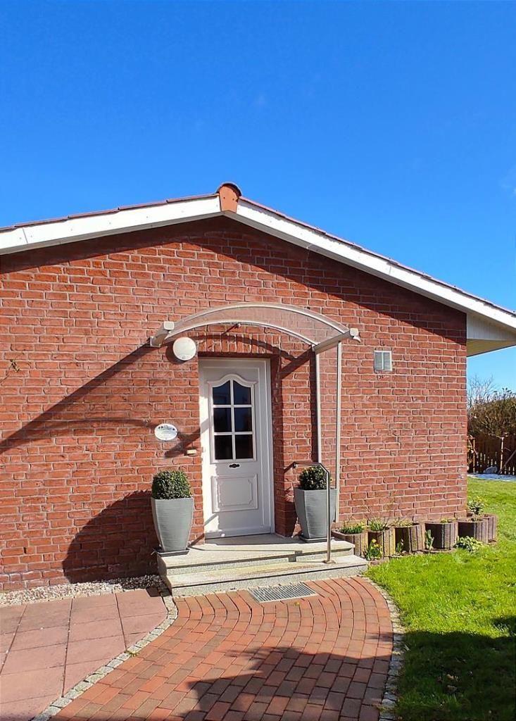 Rotes Backsteinhaus mit weißer Tür und Pflanzenbeeten.