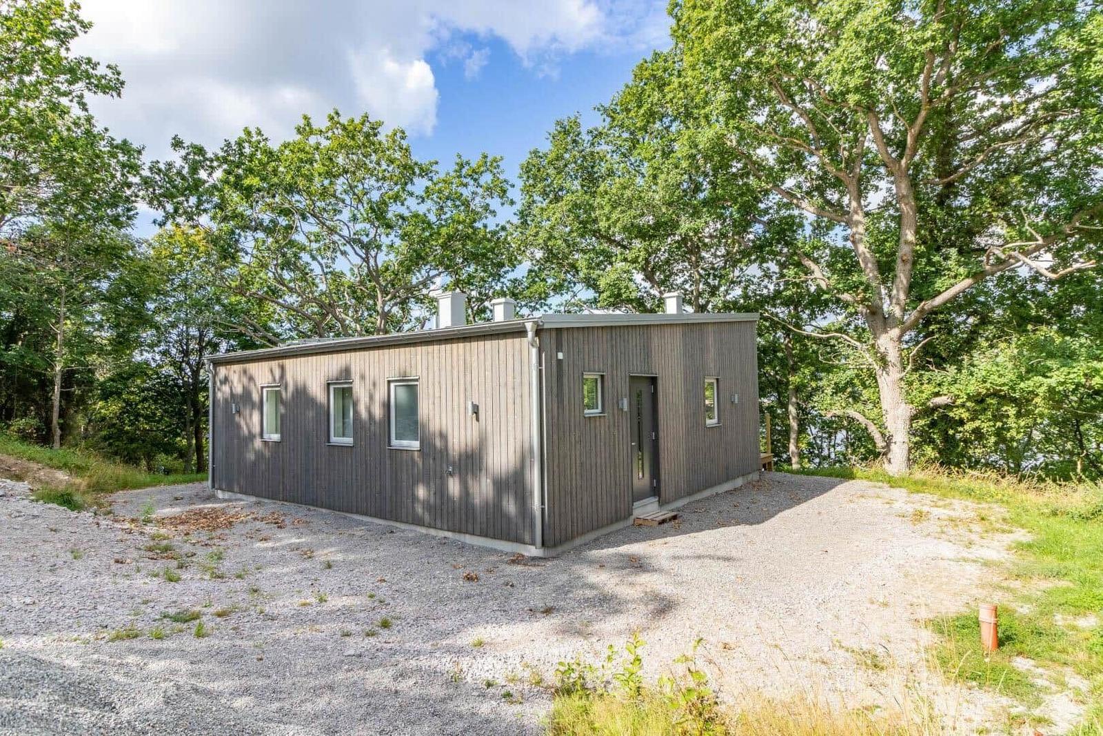 Moderne Holzhütte mit Fenstern und Tür, umgeben von Bäumen und Kies.