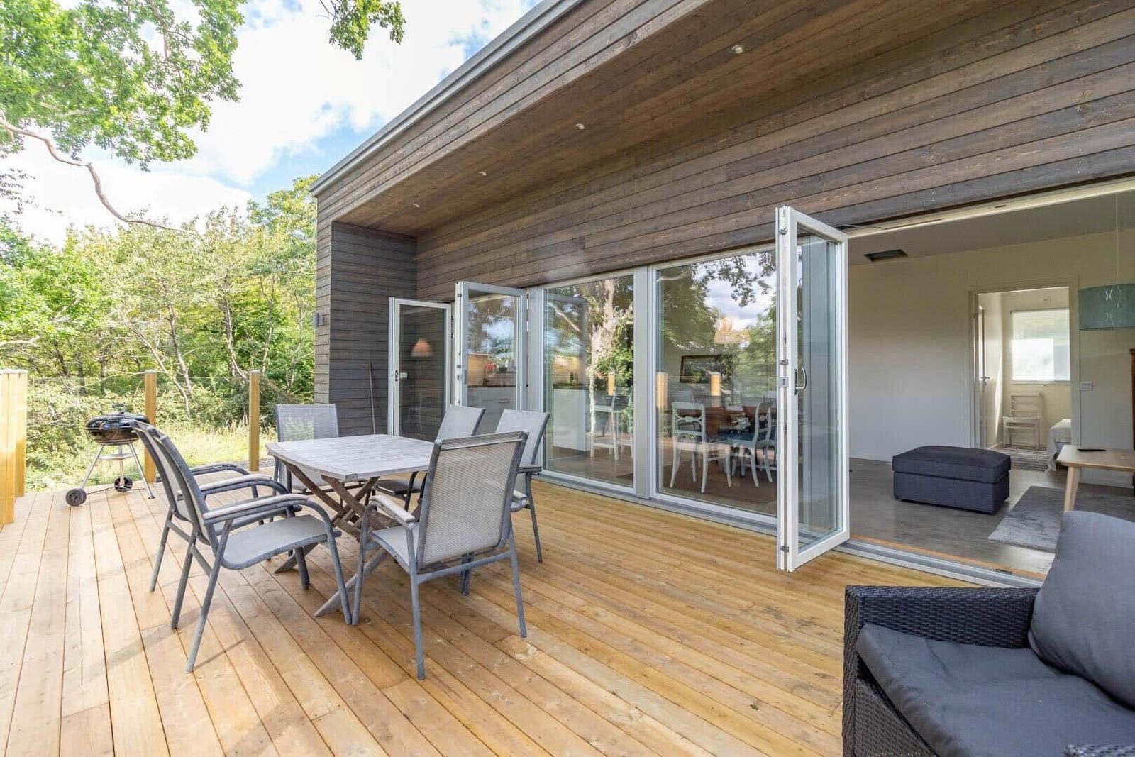 Terrasse mit Tisch, Stühlen und Grill. Durchgehende Glastüren führen ins Haus.