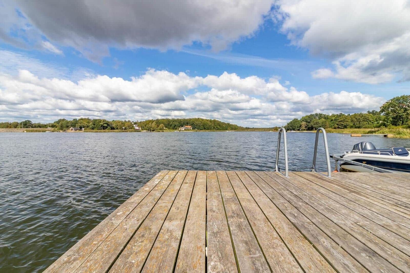 Holzsteg führt zum Wasser, Boot liegt bereit, Blick auf den See und grüne Ufer.