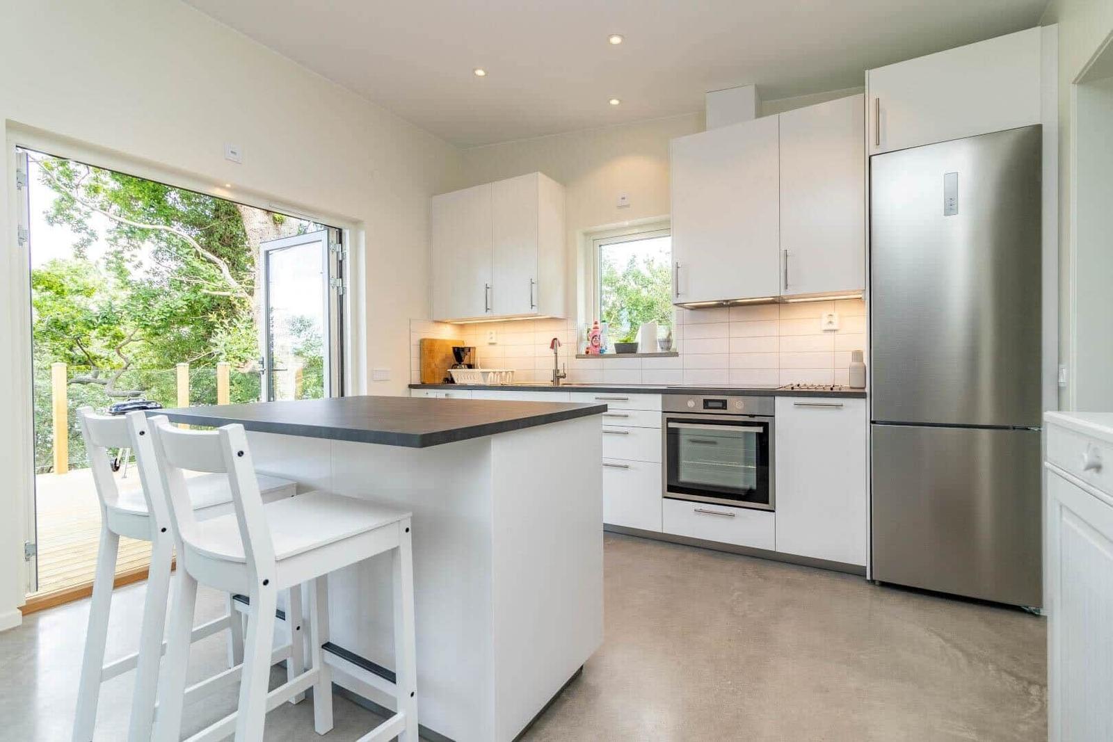 Moderne Küche mit weißer Arbeitsplatte, Edelstahlkühlschrank und Blick auf den Garten.