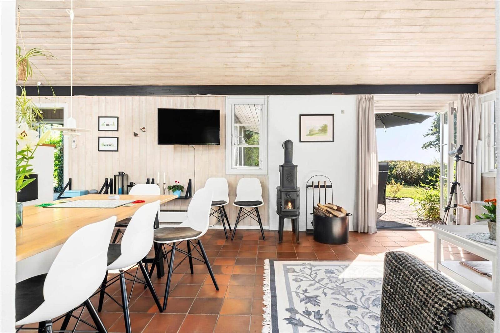 Esszimmer mit Holztisch, weißen Stühlen und Kaminofen. Durchgang zur Terrasse mit Gartenblick.