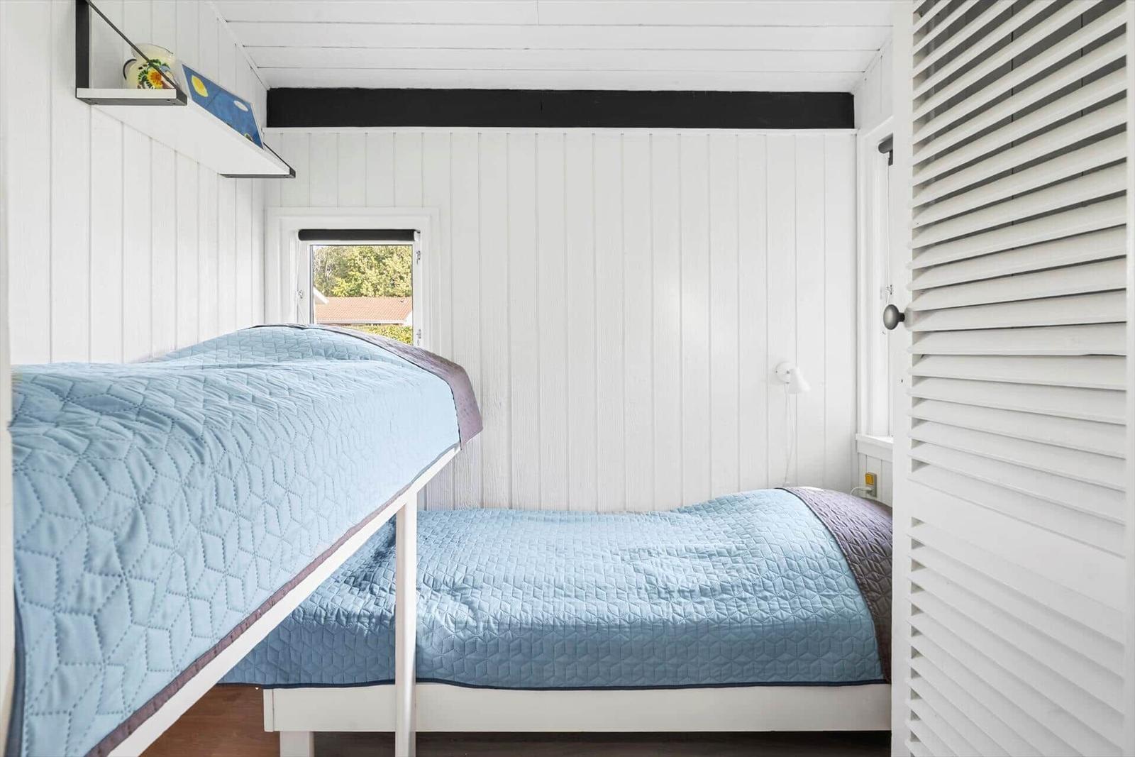 Zimmer mit Doppelstockbett, weißer Holzwand und kleinem Fenster.