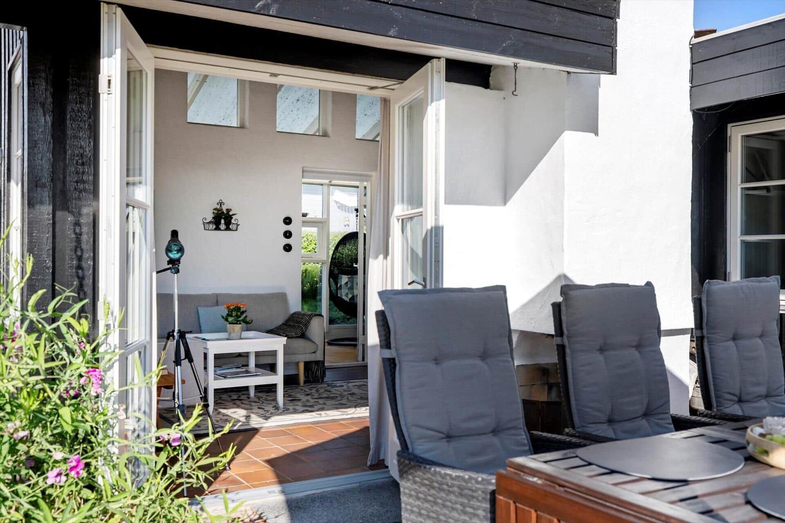 Terrasse mit Sitzgelegenheiten und Blick ins Haus. Weiße Wände und Holzboden.