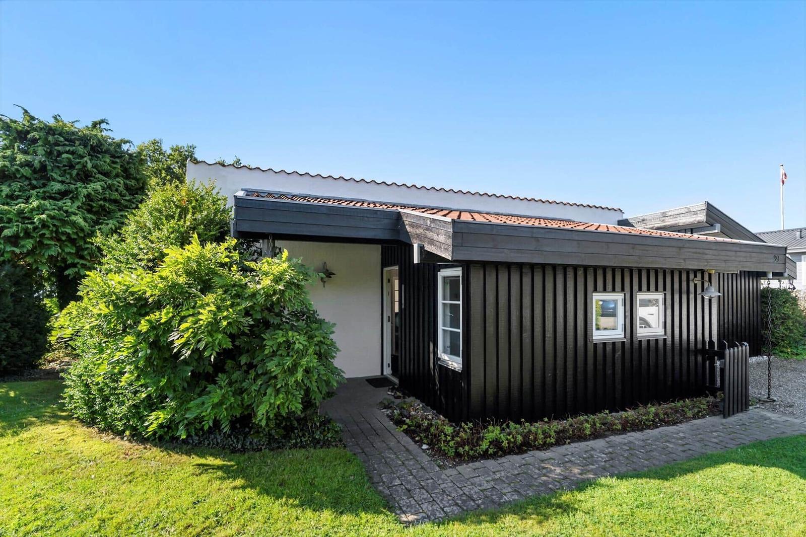 Ein Haus mit schwarzem Holzverkleidung und rotem Ziegeldach. Grünflächen und ein gepflasterter Weg.