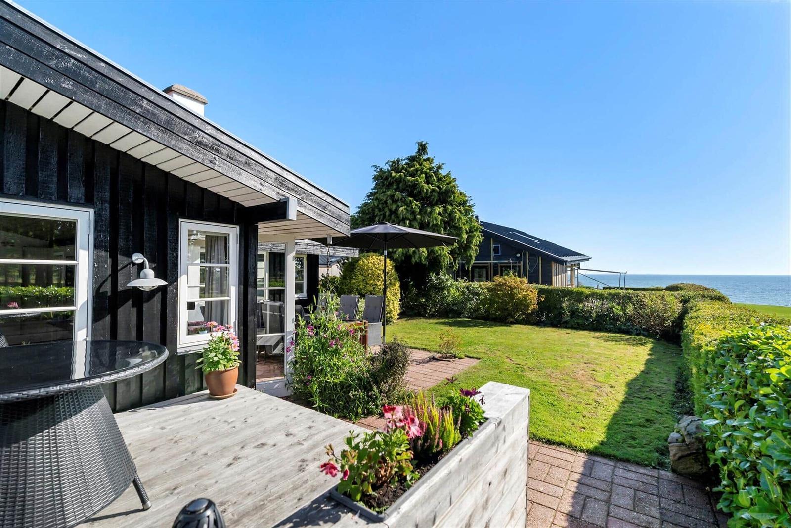 Schwarzes Holzhaus mit Terrasse, Garten und Meerblick.