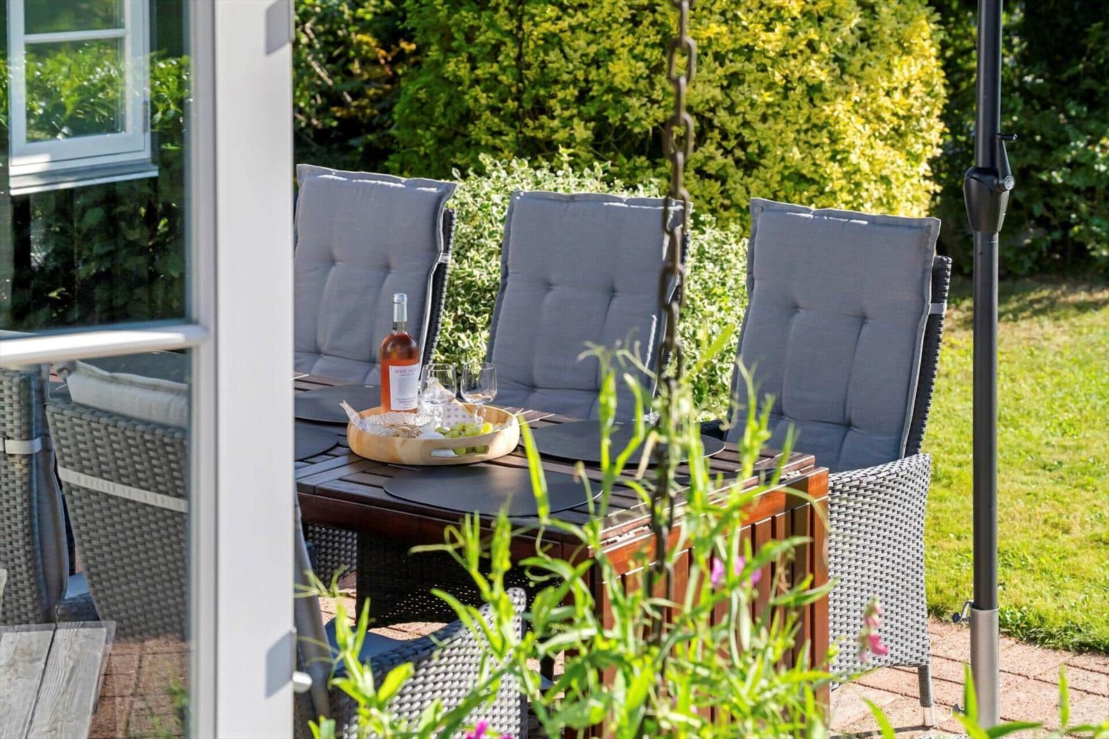 Terrasse mit Tisch, drei Stühlen und Weinset im Garten.
