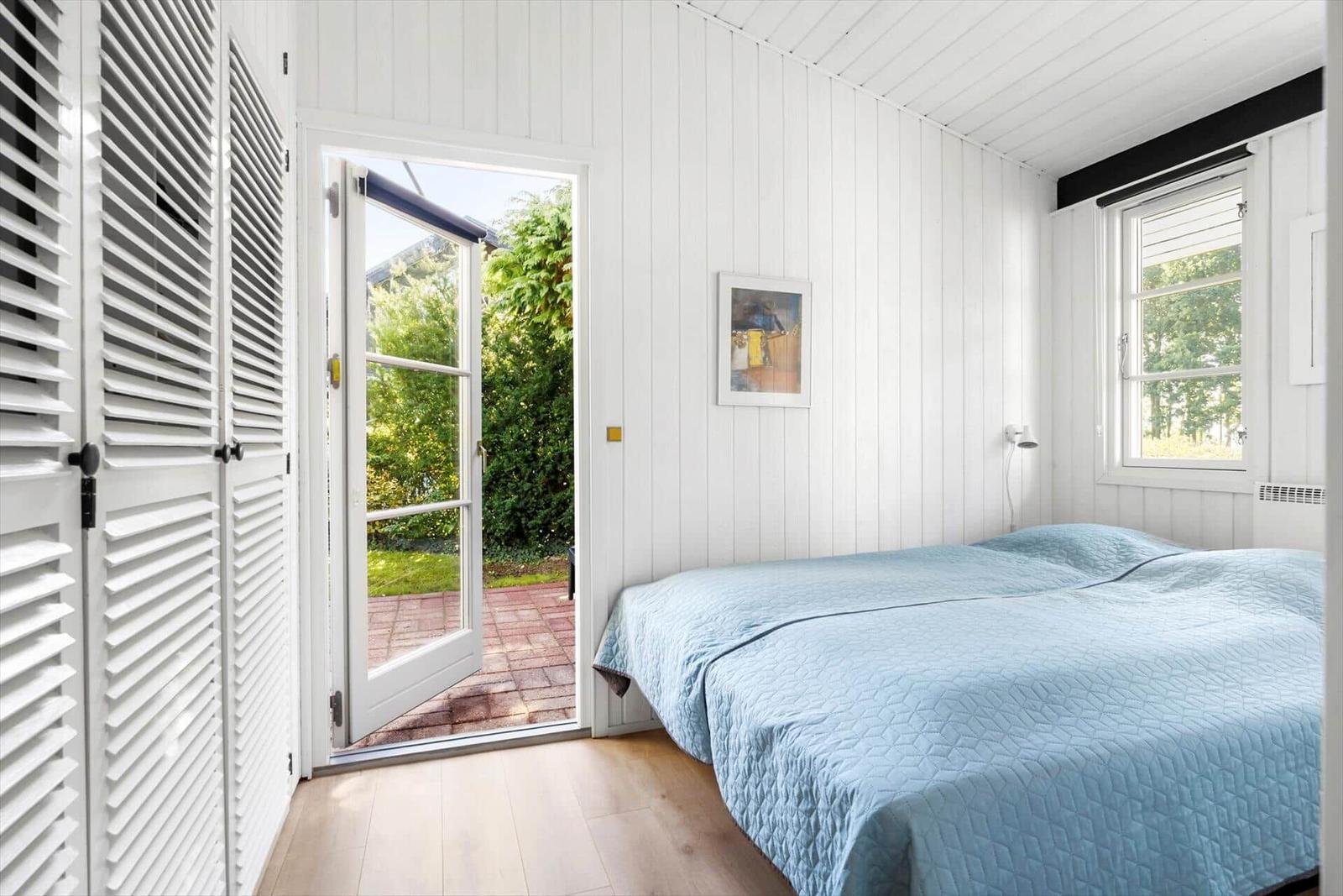 Schlafzimmer mit Bett, Tür zum Garten und Fenster mit Blick auf Grün.