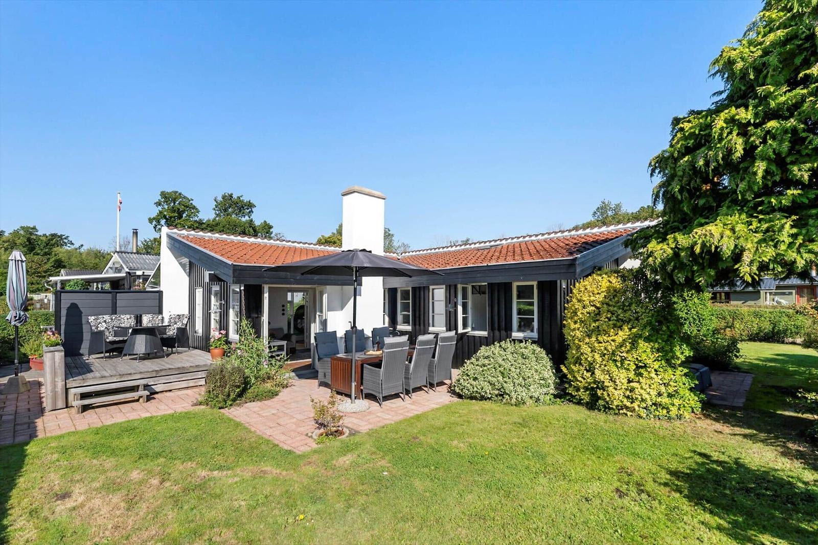 Haus mit Terrasse, Garten und Sitzgelegenheiten unter Sonnenschirm.