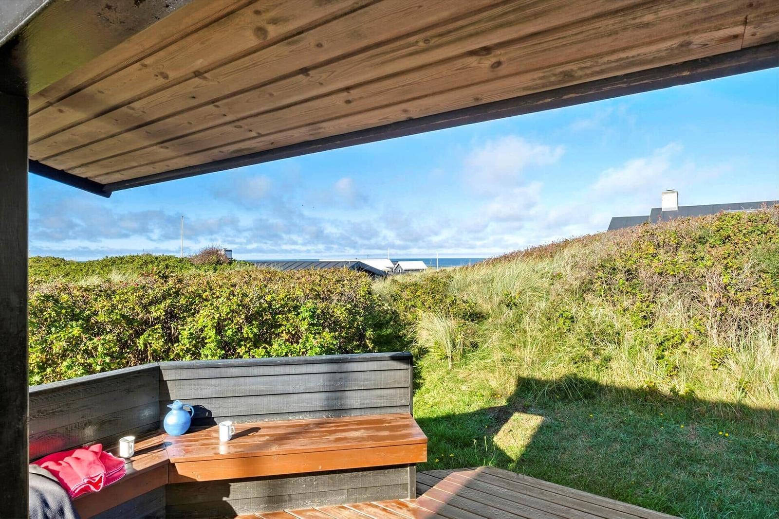 Terrasse mit Sitzbank und Blick auf Grünflächen und Meer.