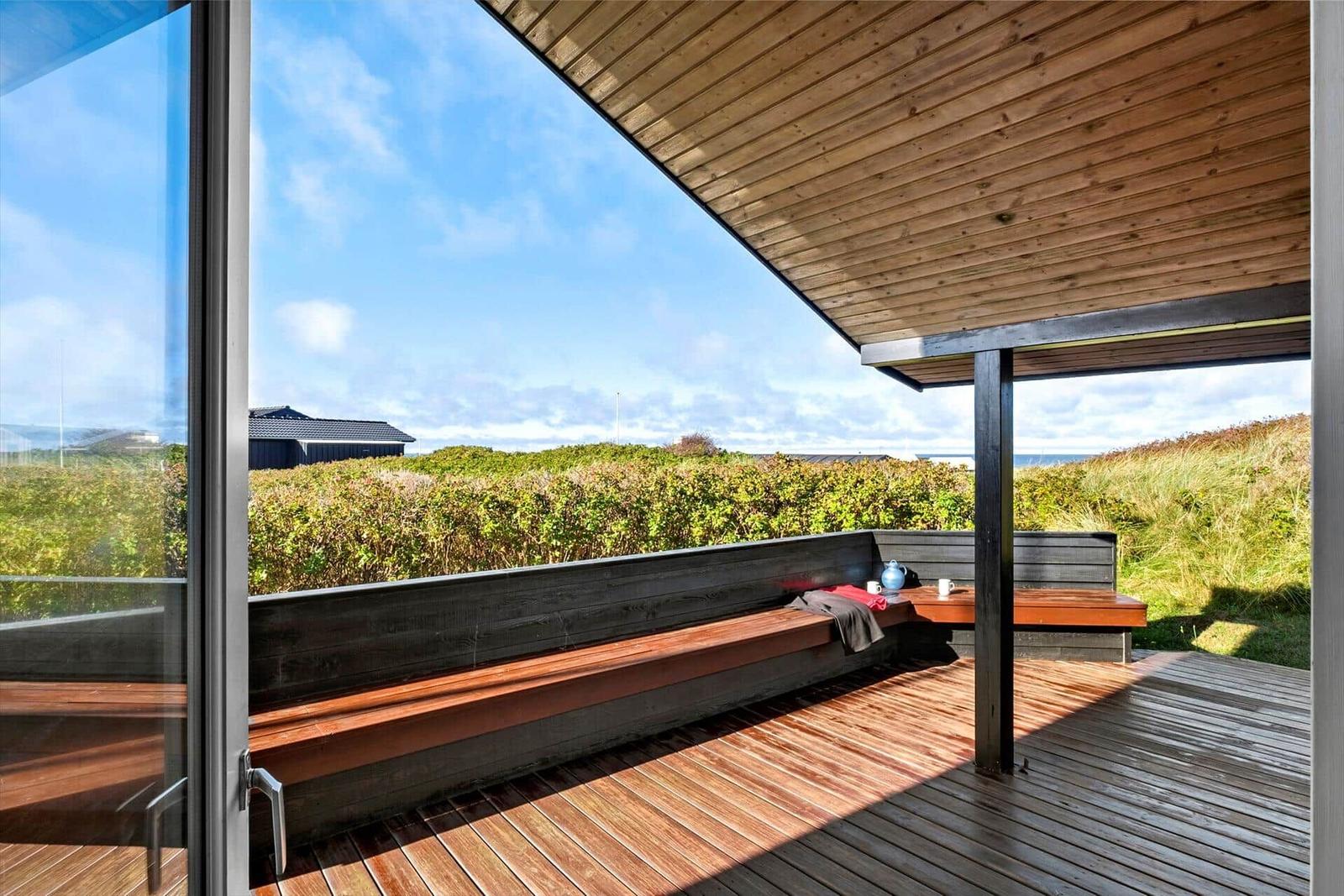 Terrasse mit Holzboden und Sitzbank. Blick auf Grünflächen und Himmel.