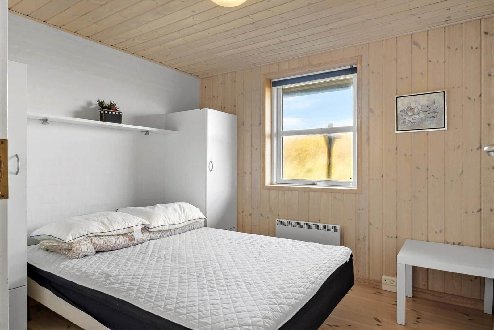 Schlafzimmer mit Bett, Kleiderschrank und Fenster.