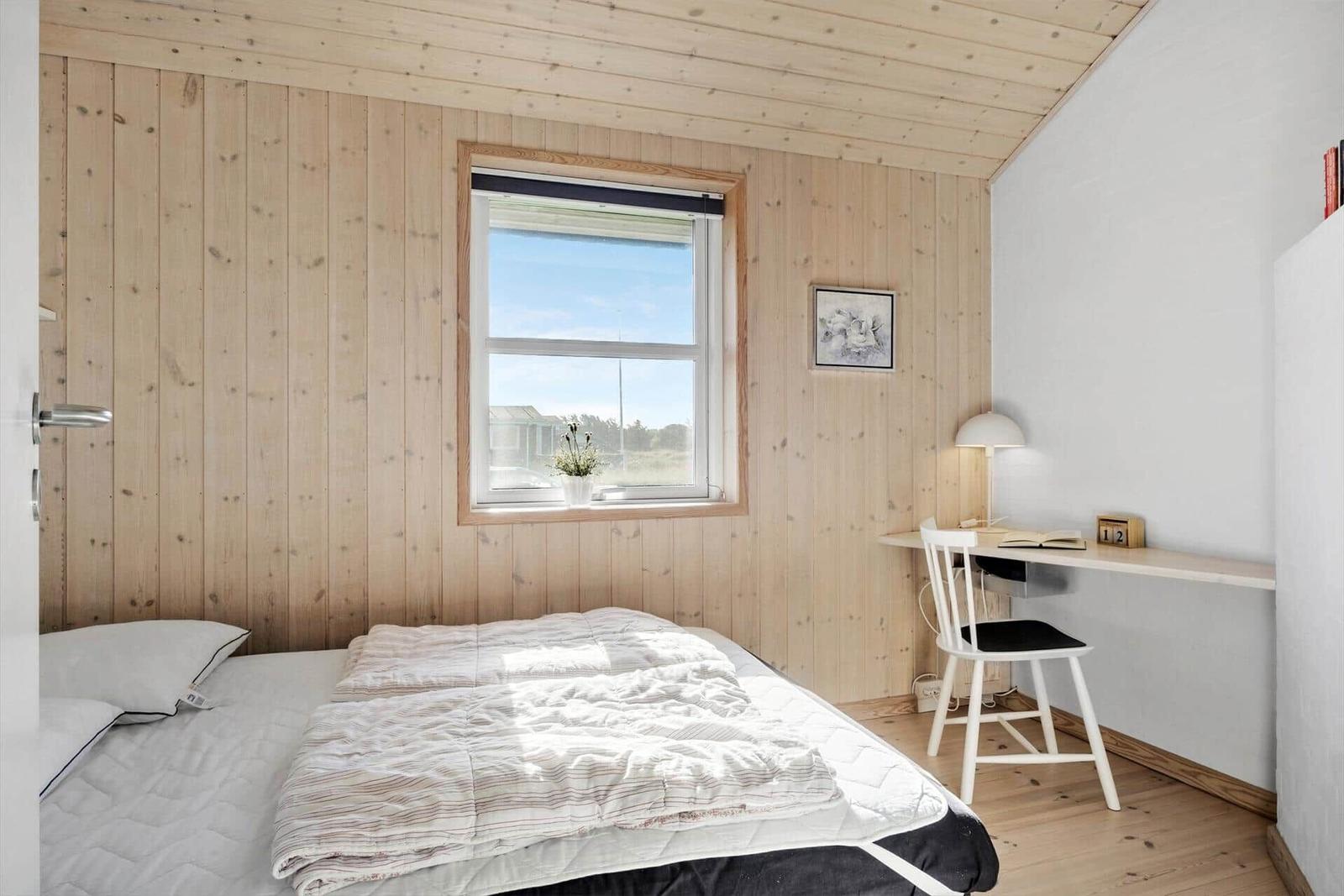 Schlafzimmer mit Bett, Schreibtisch und Fenster. Holzwand und Decke.
