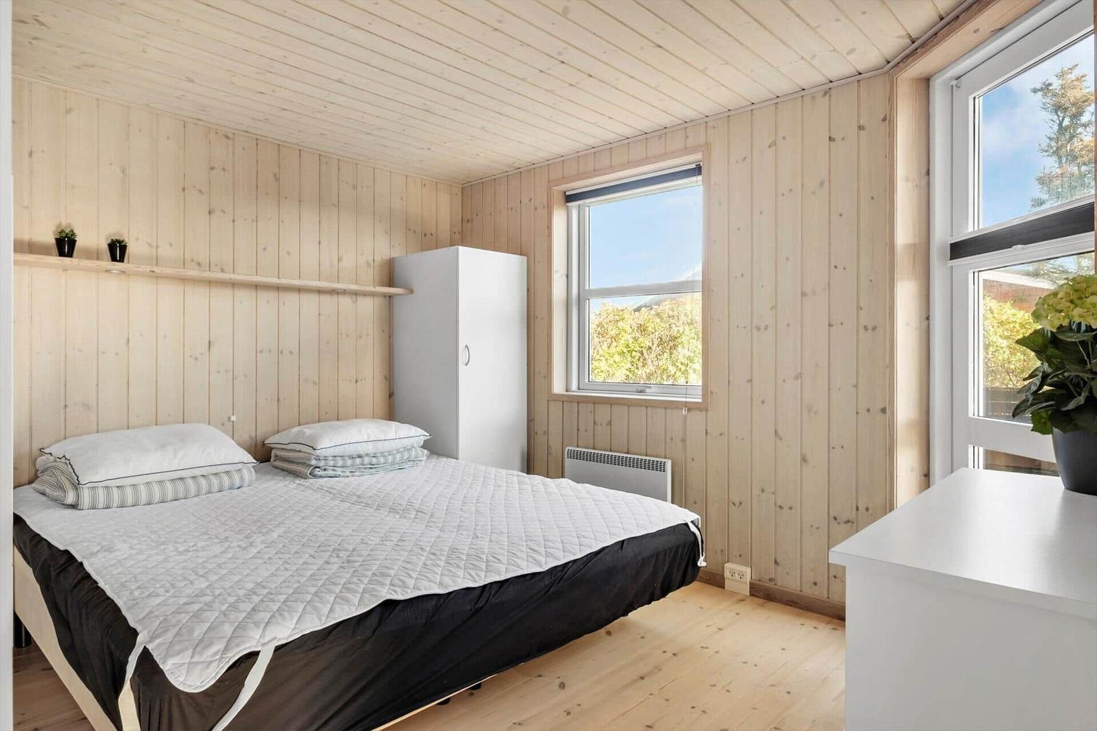 Schlafzimmer mit Holzwänden, Bett, Kleiderschrank und Fenster.