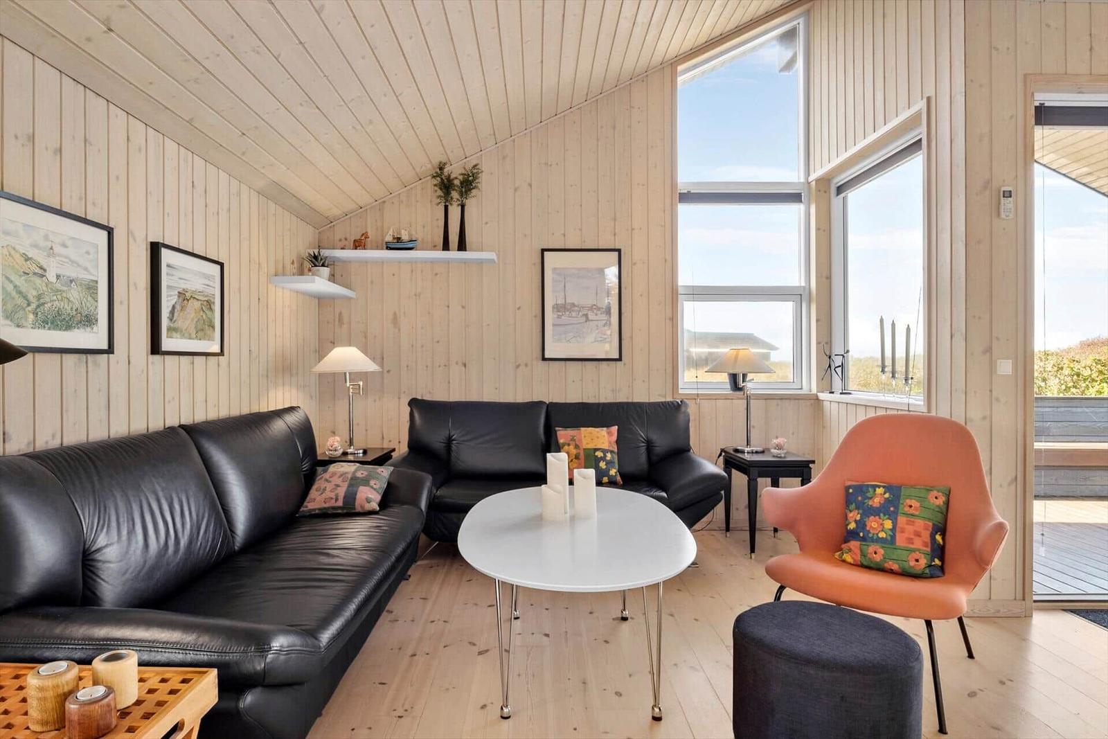 Wohnzimmer mit zwei schwarzen Sofas, orangefarbener Sessel und weißem Tisch.