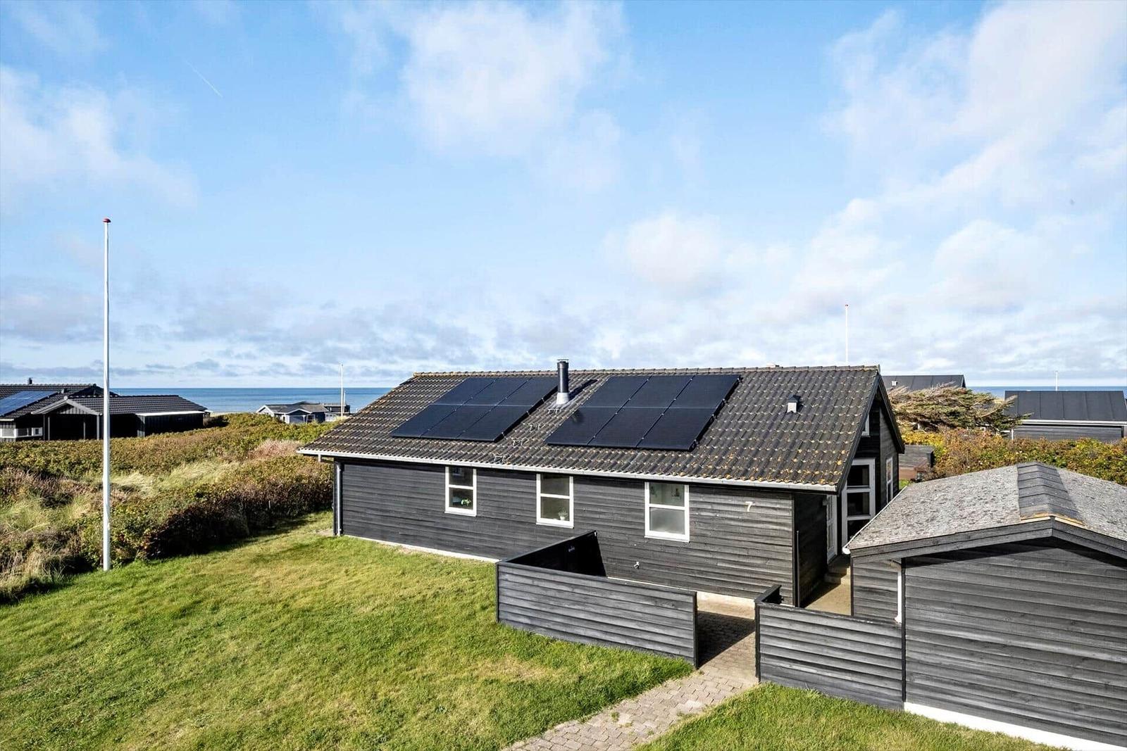 Ein Haus mit Solarpaneelen auf dem Dach, umgeben von Gras und Blick aufs Meer.