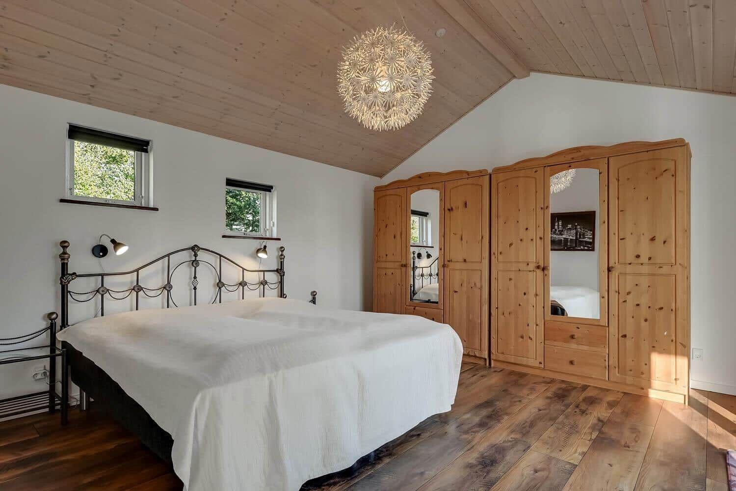 Bedroom with wooden floor, wooden ceiling, and large wardrobe with mirrors.