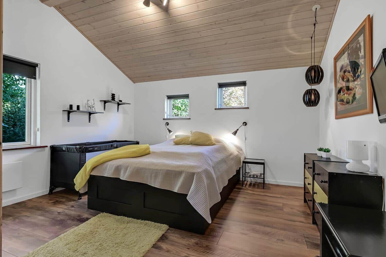 Bedroom with wooden ceiling, bed, dresser, and windows.
