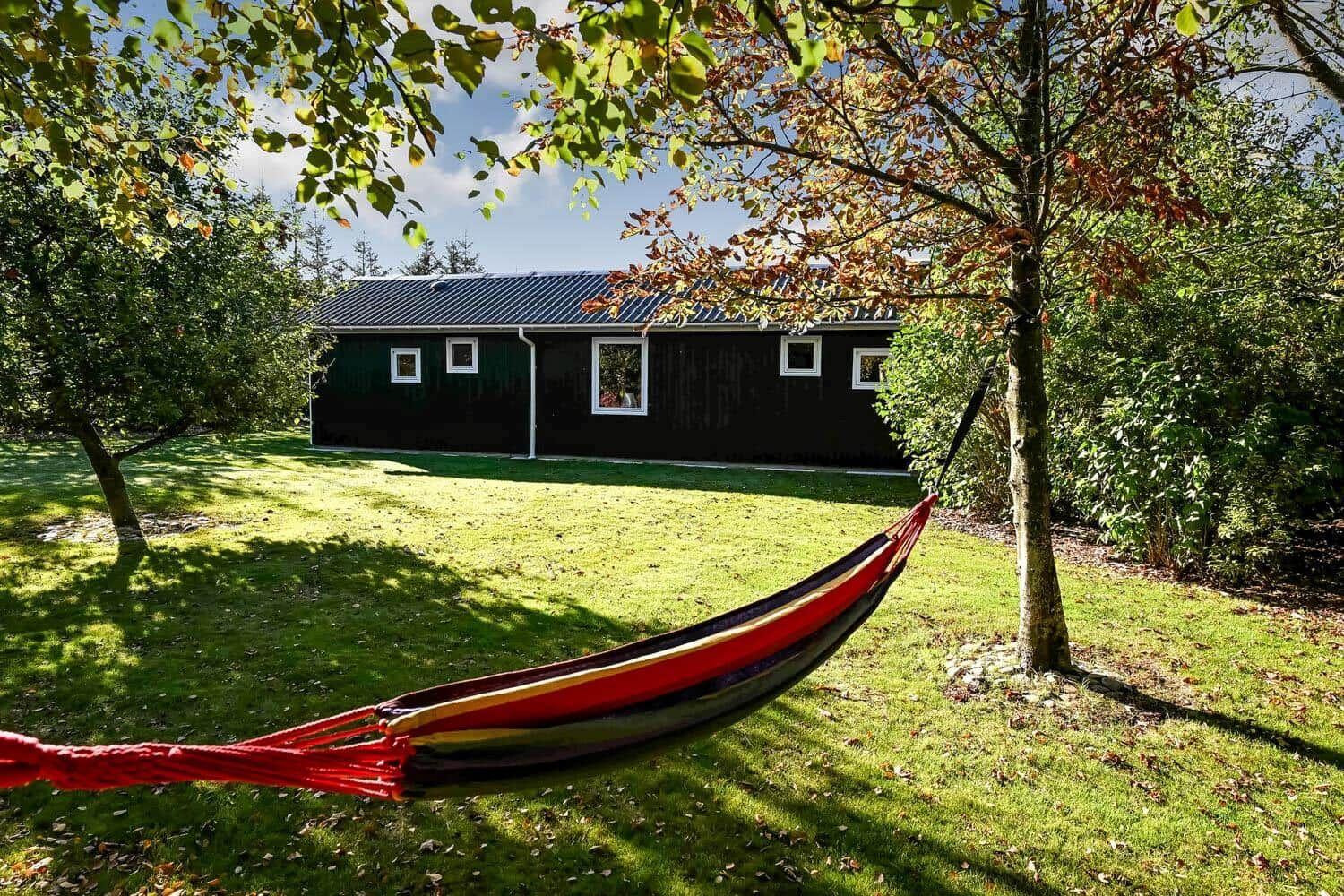A red hammock suspended before a dark wooden house with green lawn.