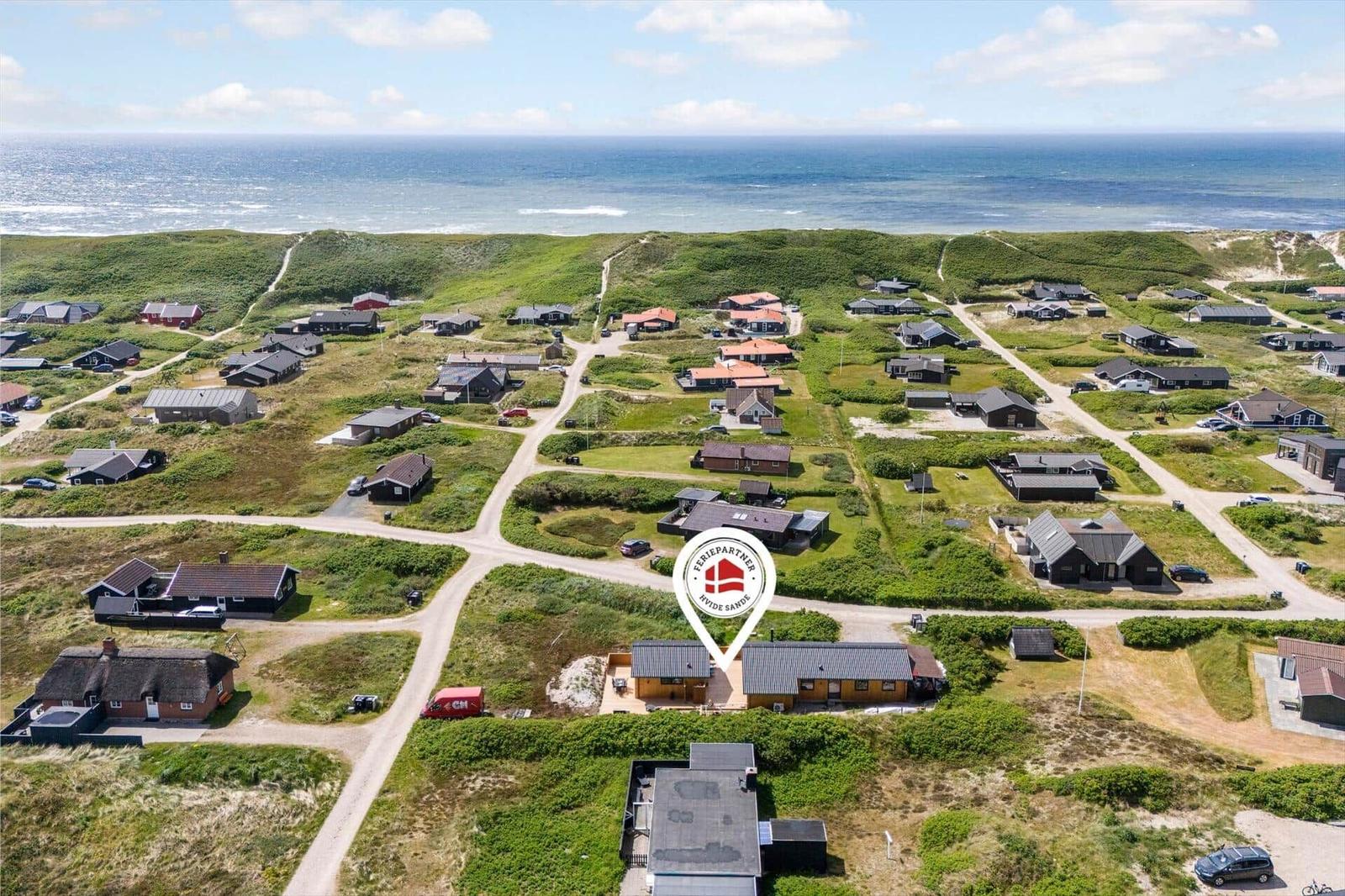 Luftbild von Ferienhäusern an der Küste mit grünen Dünen und Meer im Hintergrund.
