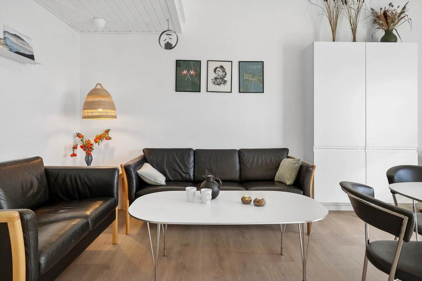 Wohnzimmer mit Ledersofa, weißem Tisch und Wandbildern.