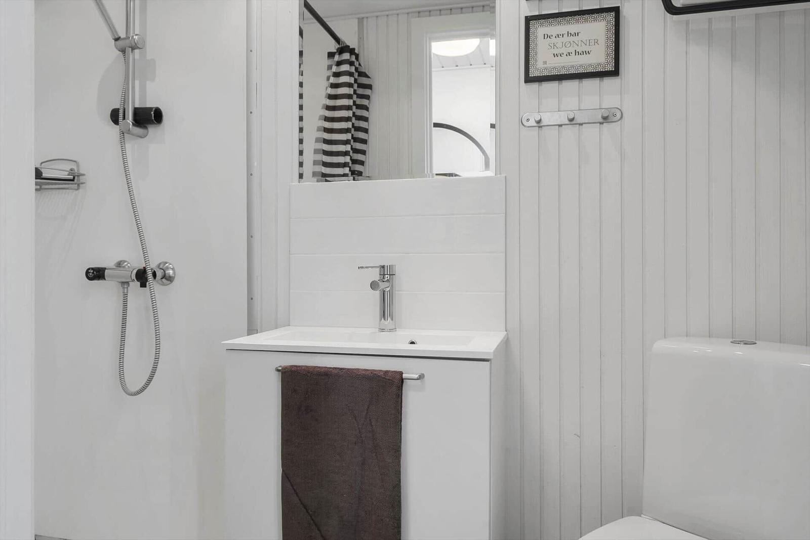 Badezimmer mit Dusche, Waschbecken und Toilette. Weiße Wände und ein brauner Handtuch.