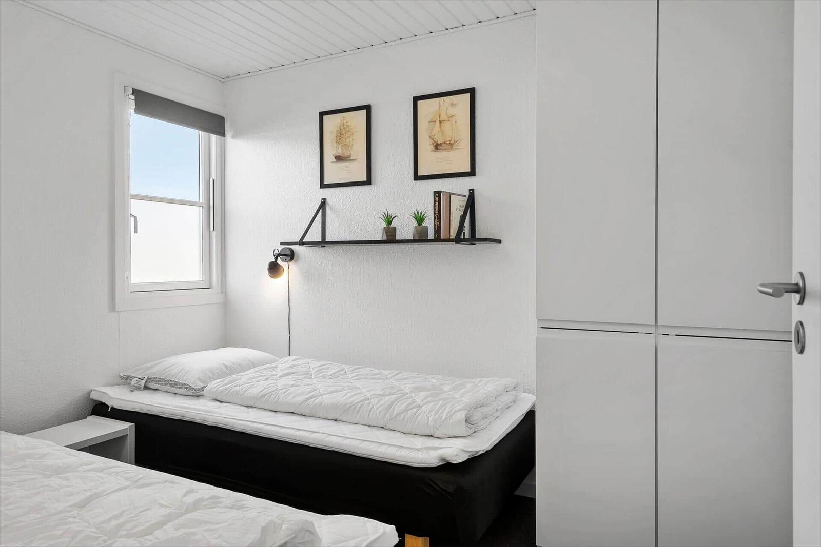Zimmer mit Bett, Fenster, Wandregal und Kleiderschrank.