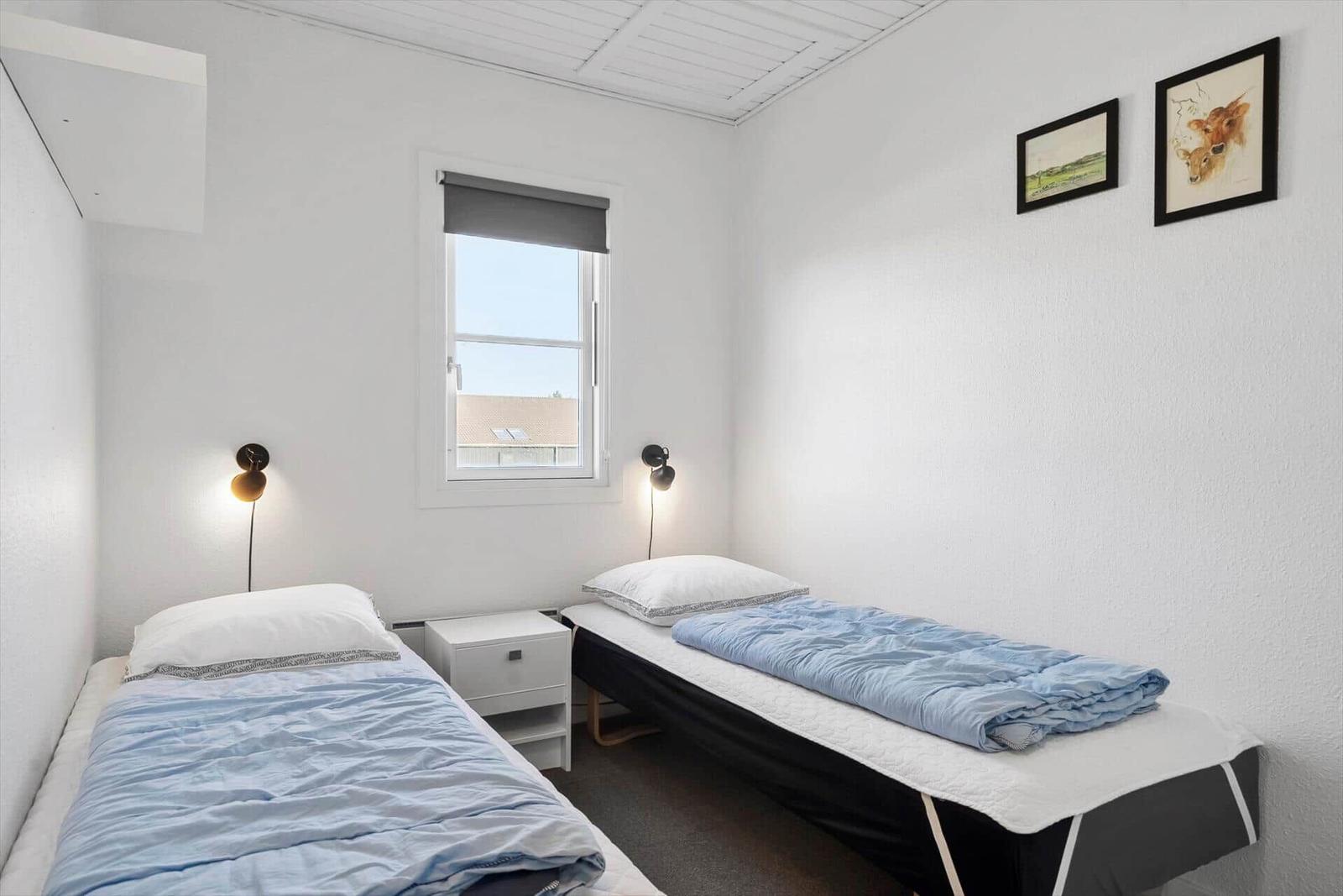Zwei Einzelbetten mit blauen Bettwäsche, Nachttisch und Fenster.