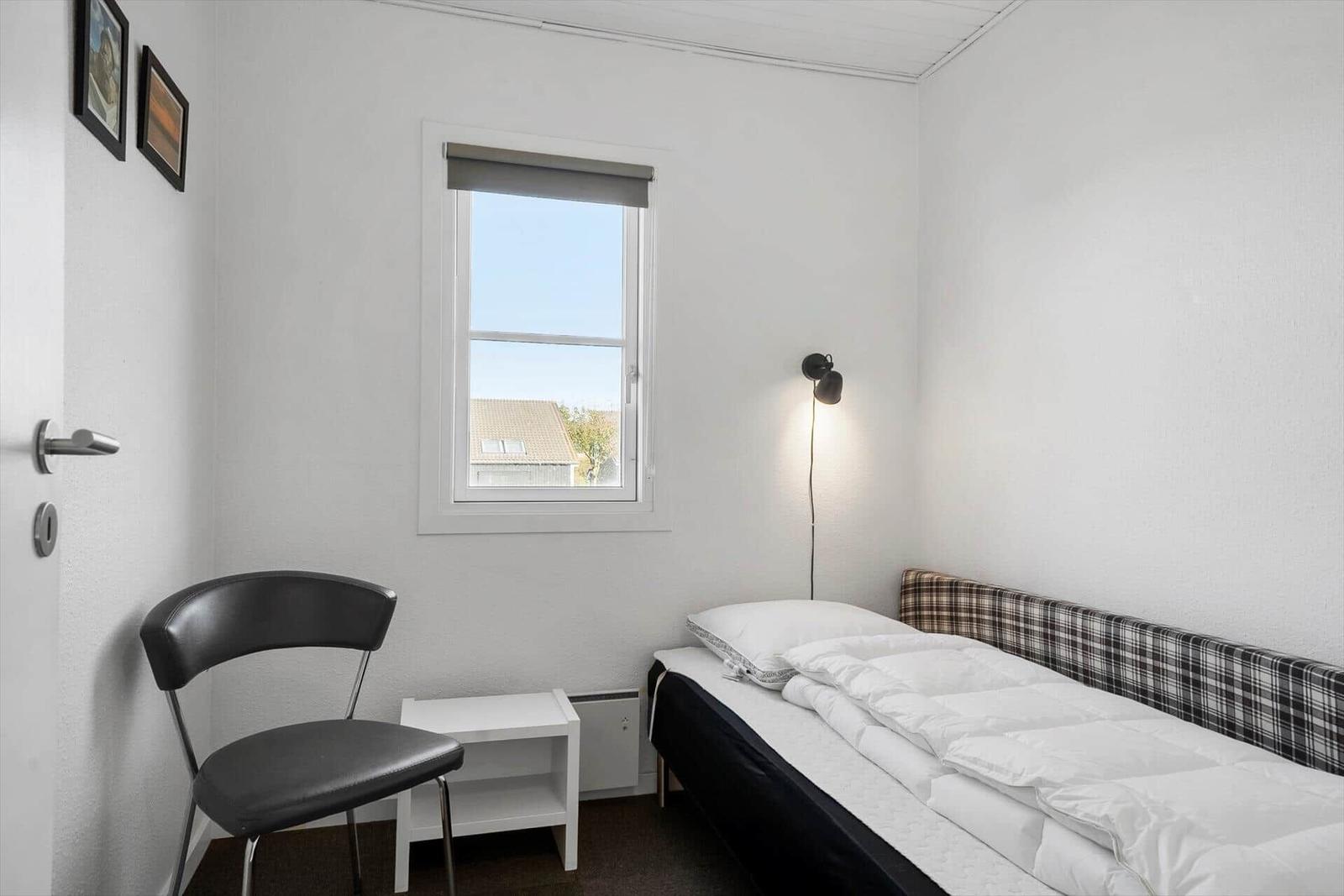 Schlafzimmer mit Bett, Stuhl und Fenster. Wandlampe und Bilder an der Wand.