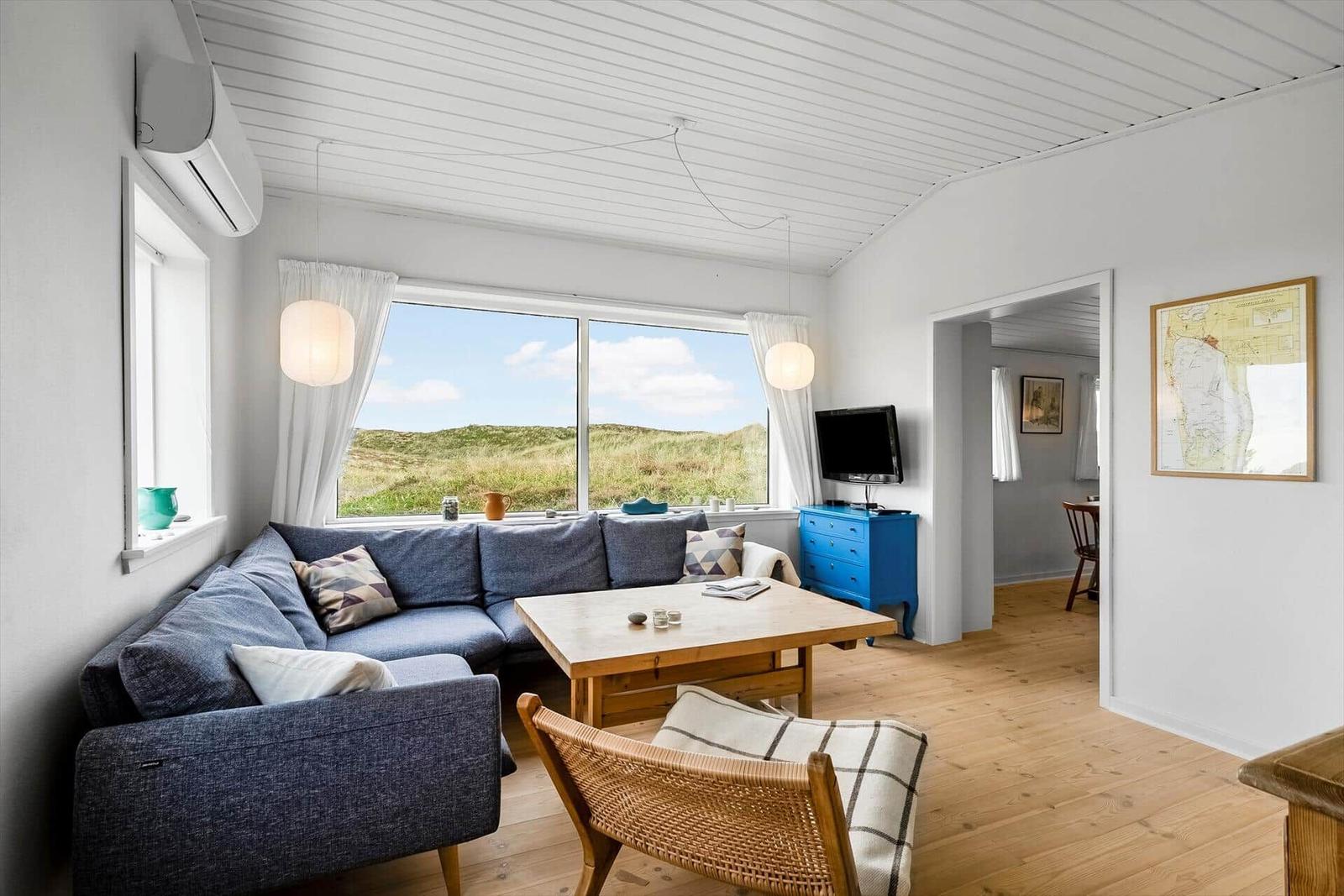 Wohnzimmer mit Sofa, Tisch und Blick auf Dünen.