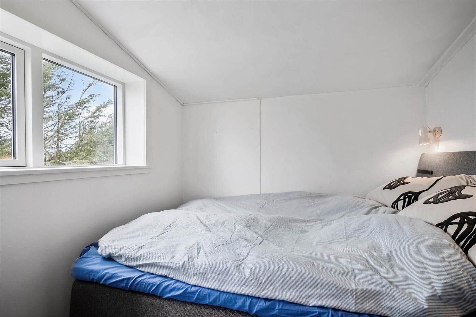 Schlafzimmer mit Bett, Fenster und Wandlampe