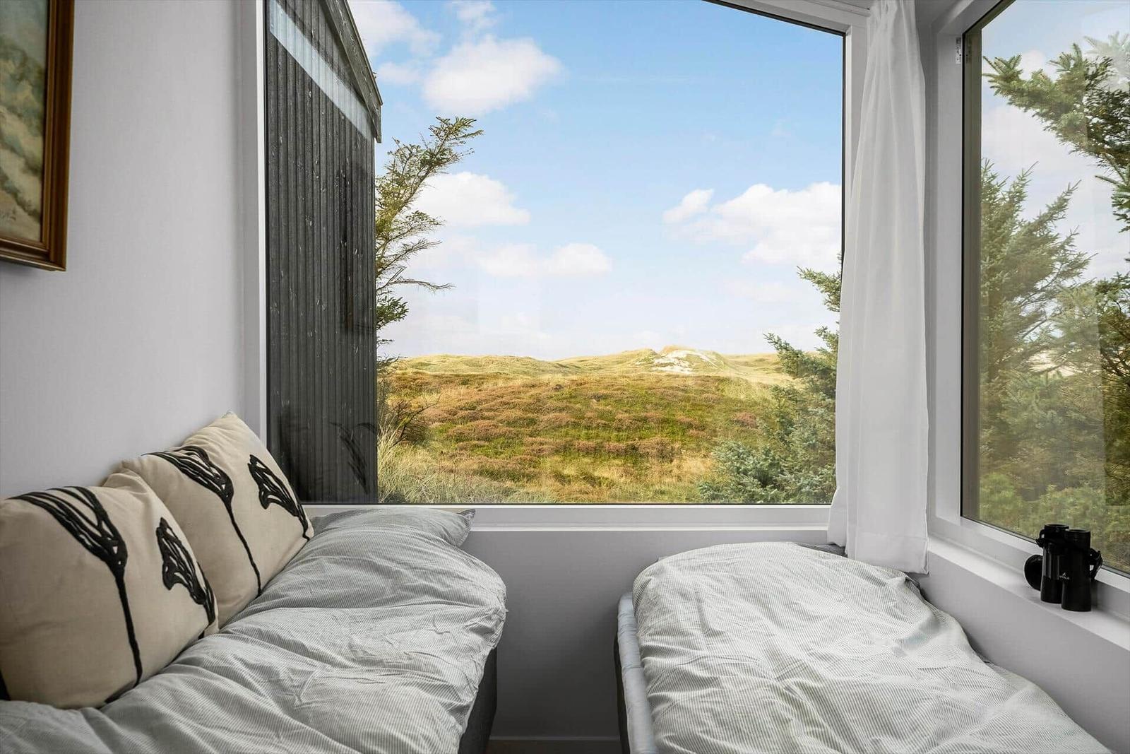 Zwei Betten mit Blick auf Hügel und Bäume durch große Fenster.