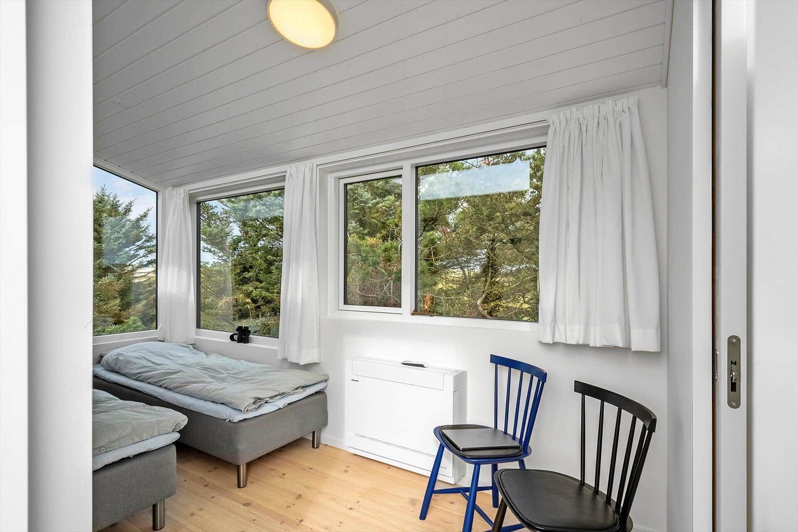 Zimmer mit zwei Betten, Fenstern und Stühlen.