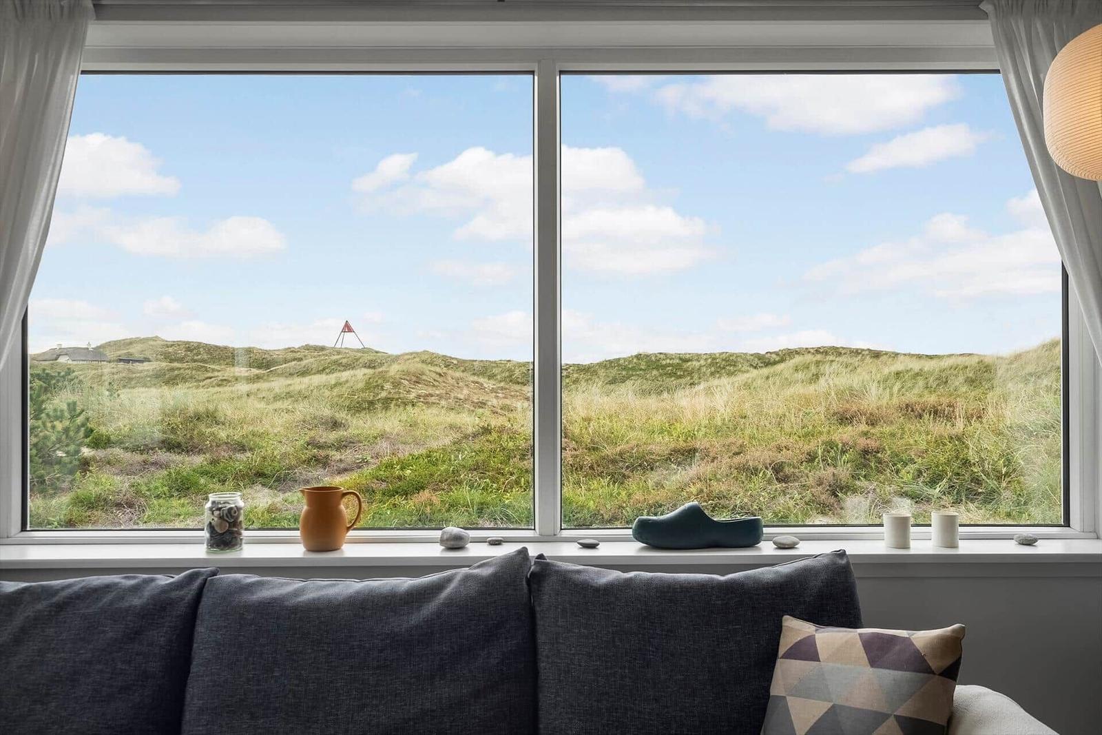 Ein Fenster mit Blick auf Dünenlandschaft. Auf dem Sims stehen ein Krug, eine Schale und ein Schuh.