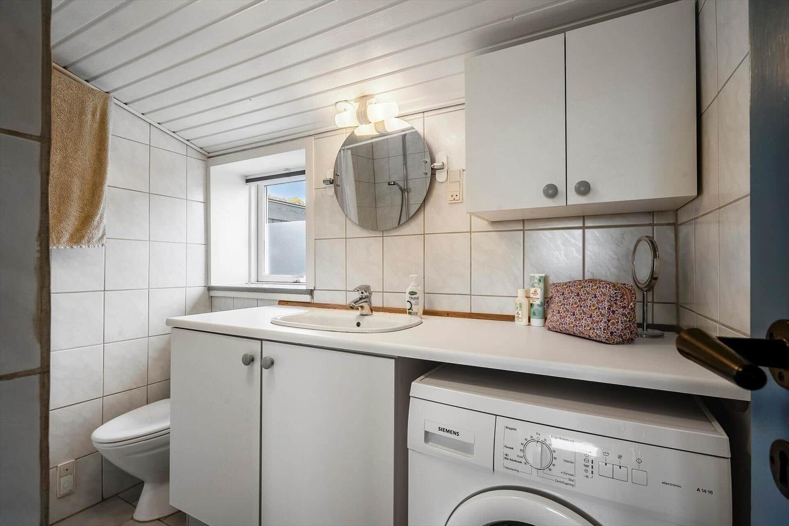 Badezimmer mit Waschmaschine, Spiegeln und Fenster.