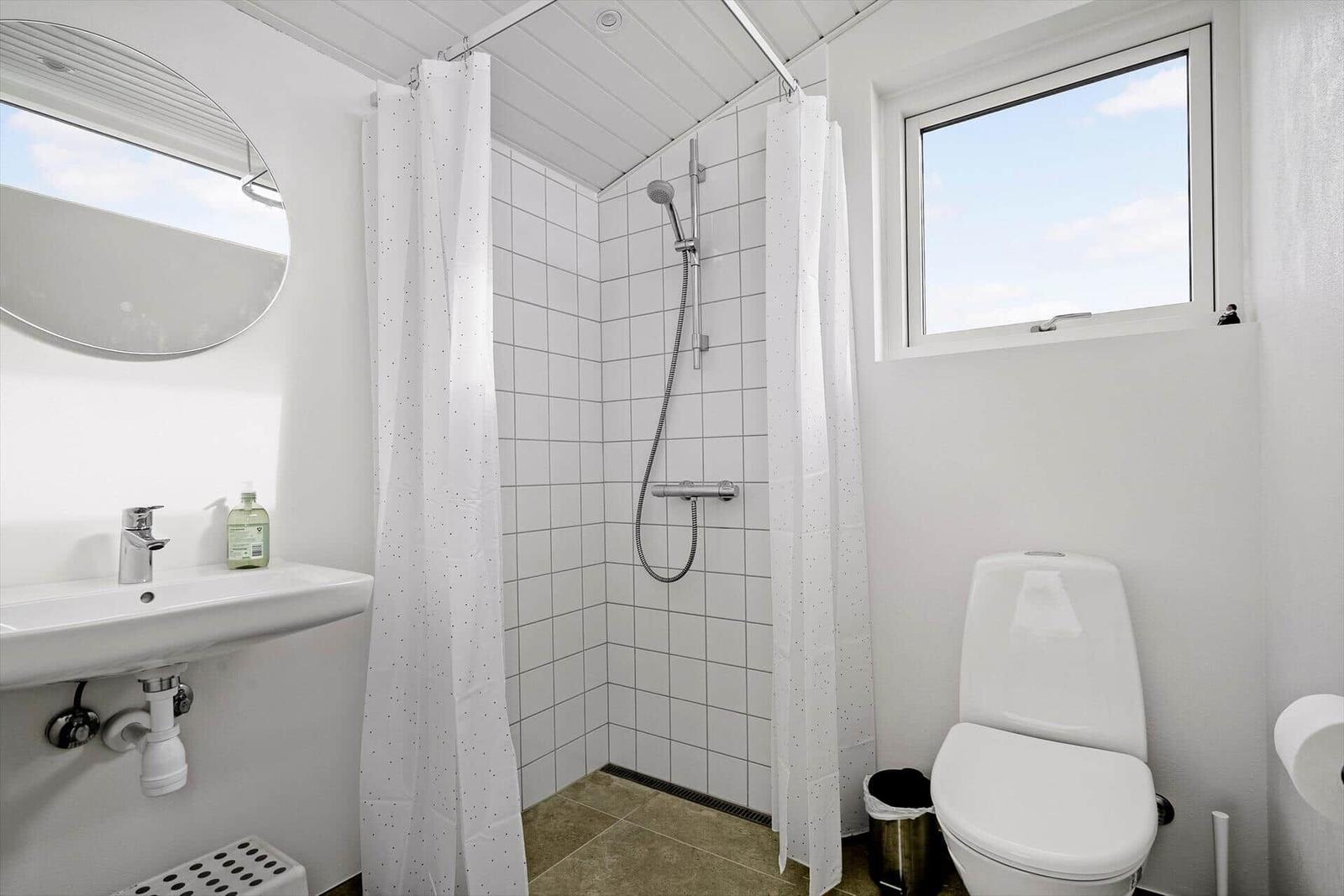Badezimmer mit Dusche, Toilette und Waschbecken. Fenster und Spiegel sichtbar.