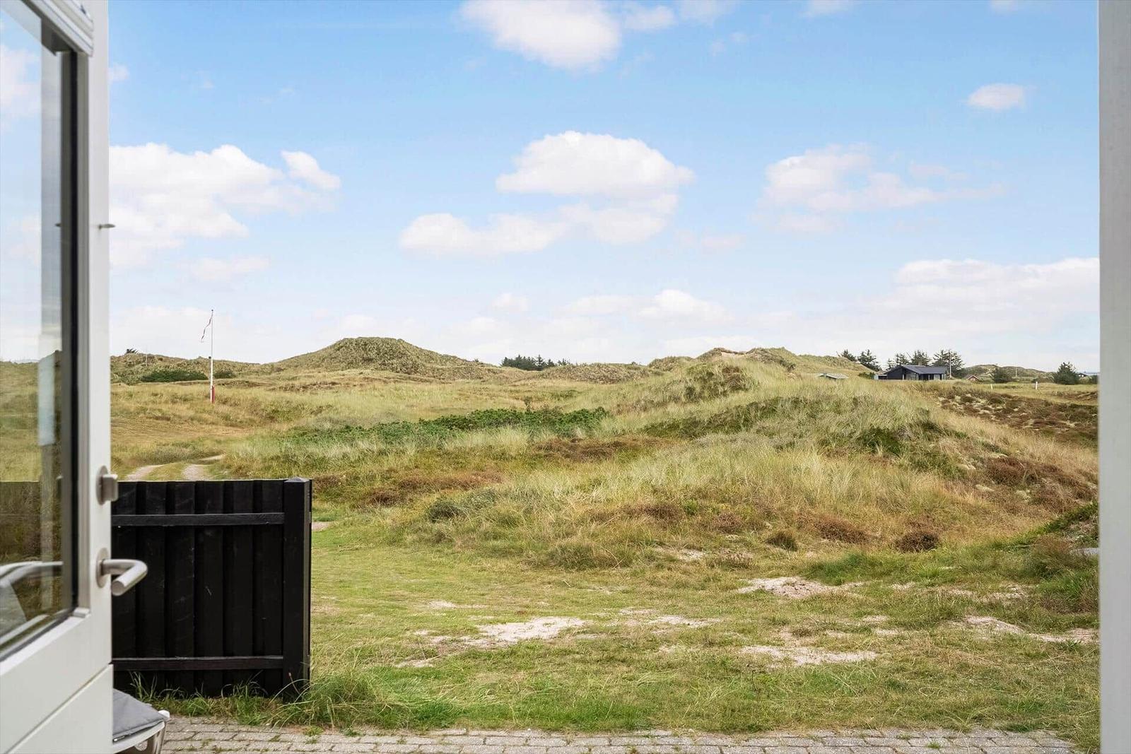 Dünenlandschaft mit Gras und einem schwarzen Zaun vor einem Fenster.