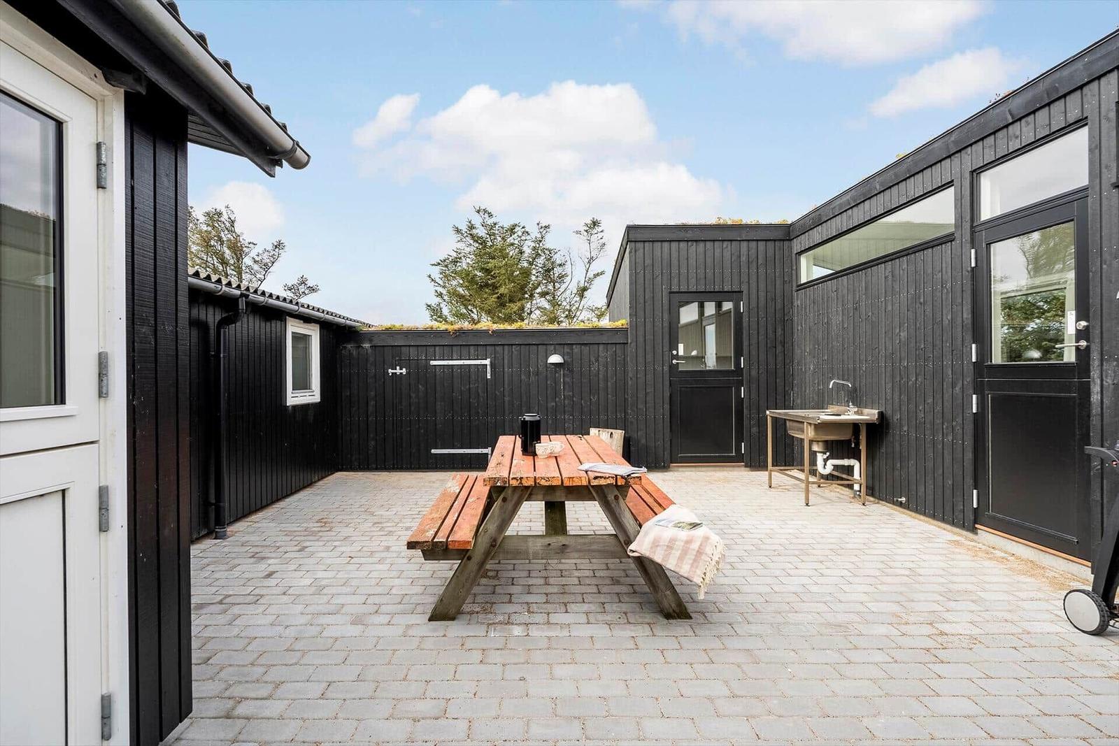 Hinterhof mit Picknicktisch, Waschbecken und schwarzen Holzwänden.