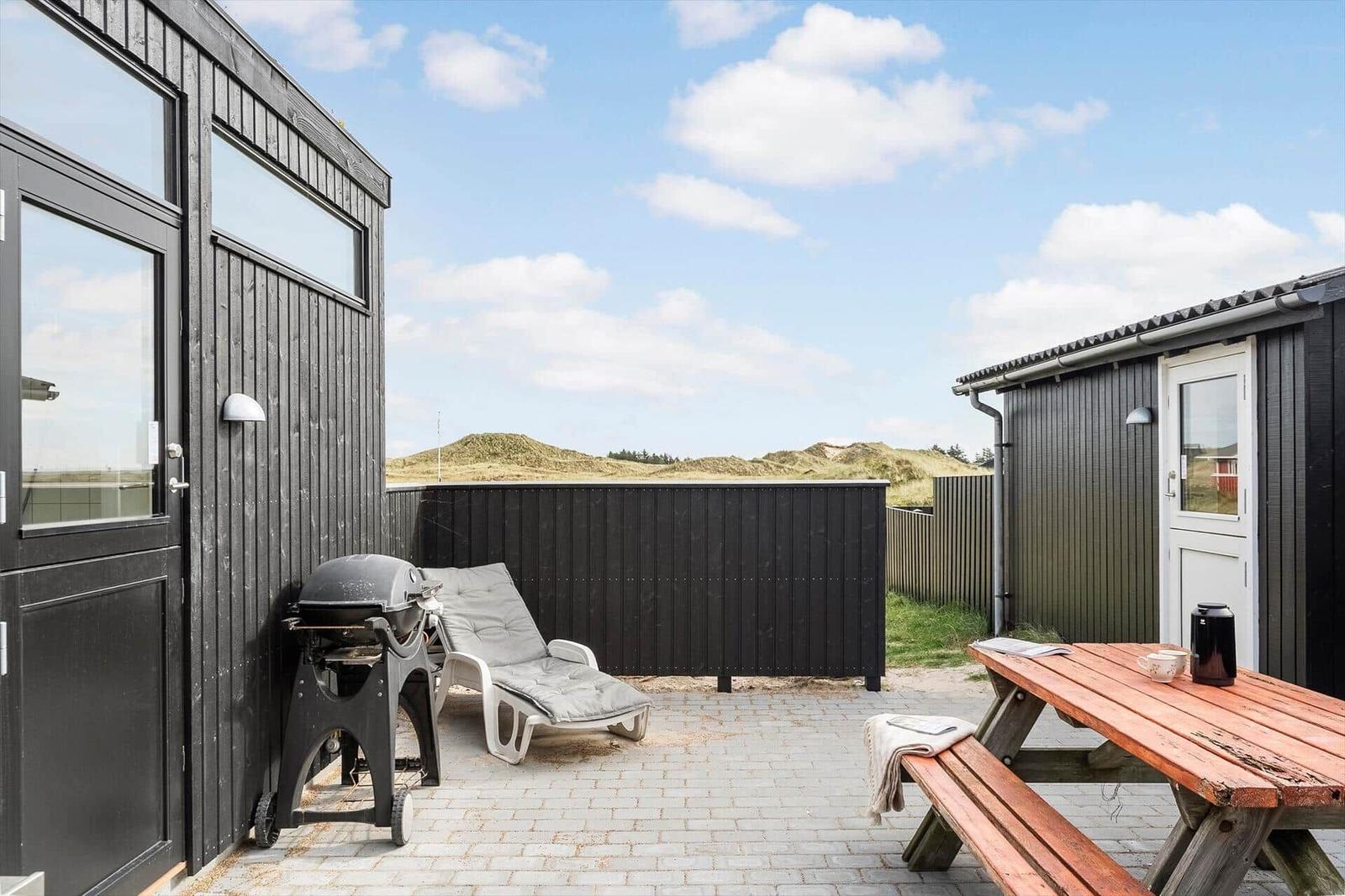 Terrasse mit Grill, Liegestuhl und Holztisch. Blick auf Dünen.