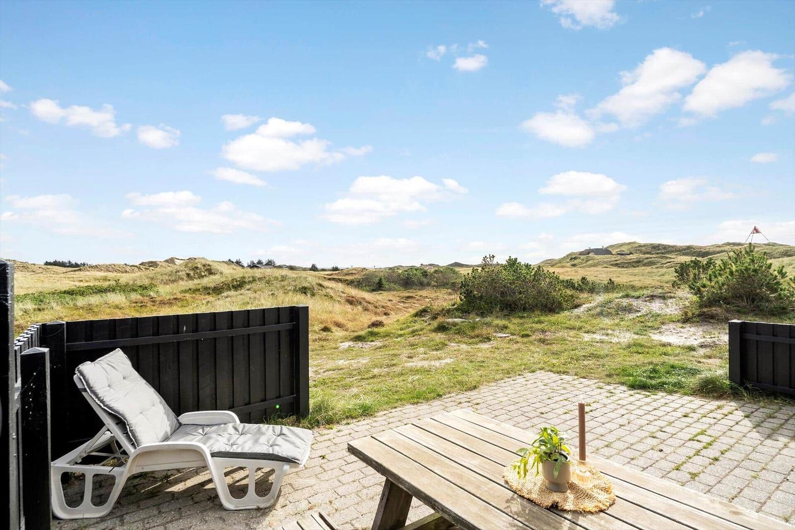 Terrasse mit Liegestuhl und Tisch. Blick auf Dünen und Himmel.