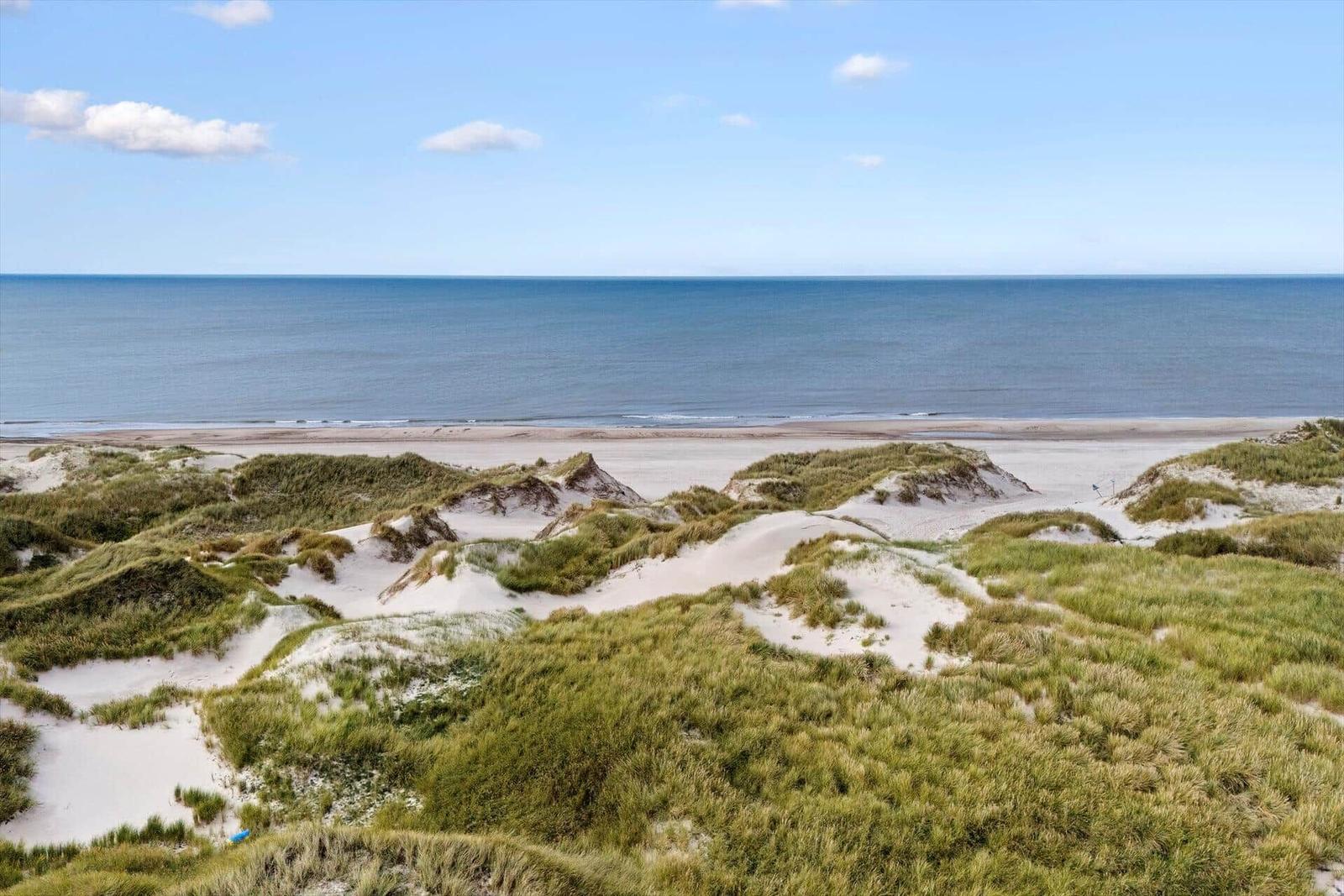 Weitläufiger Blick auf Strand und Meer mit Dünen im Vordergrund.
