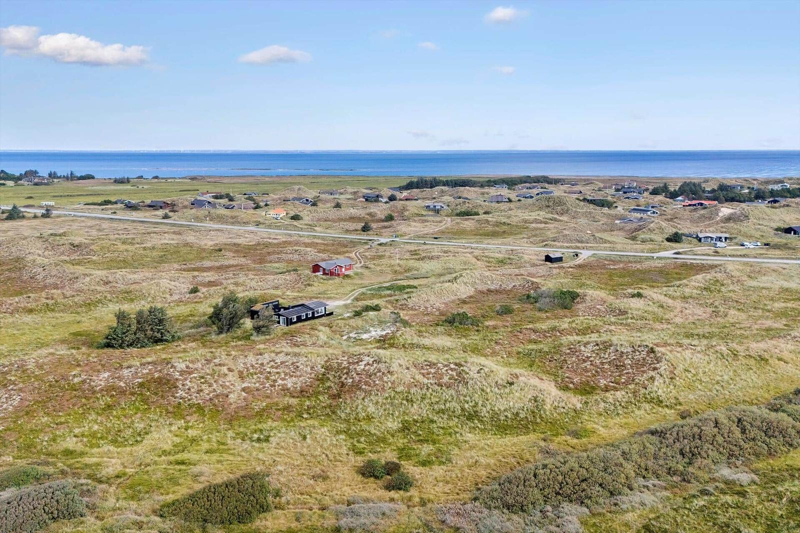 Ausblick auf Dünenlandschaft mit Häusern und Meer im Hintergrund.