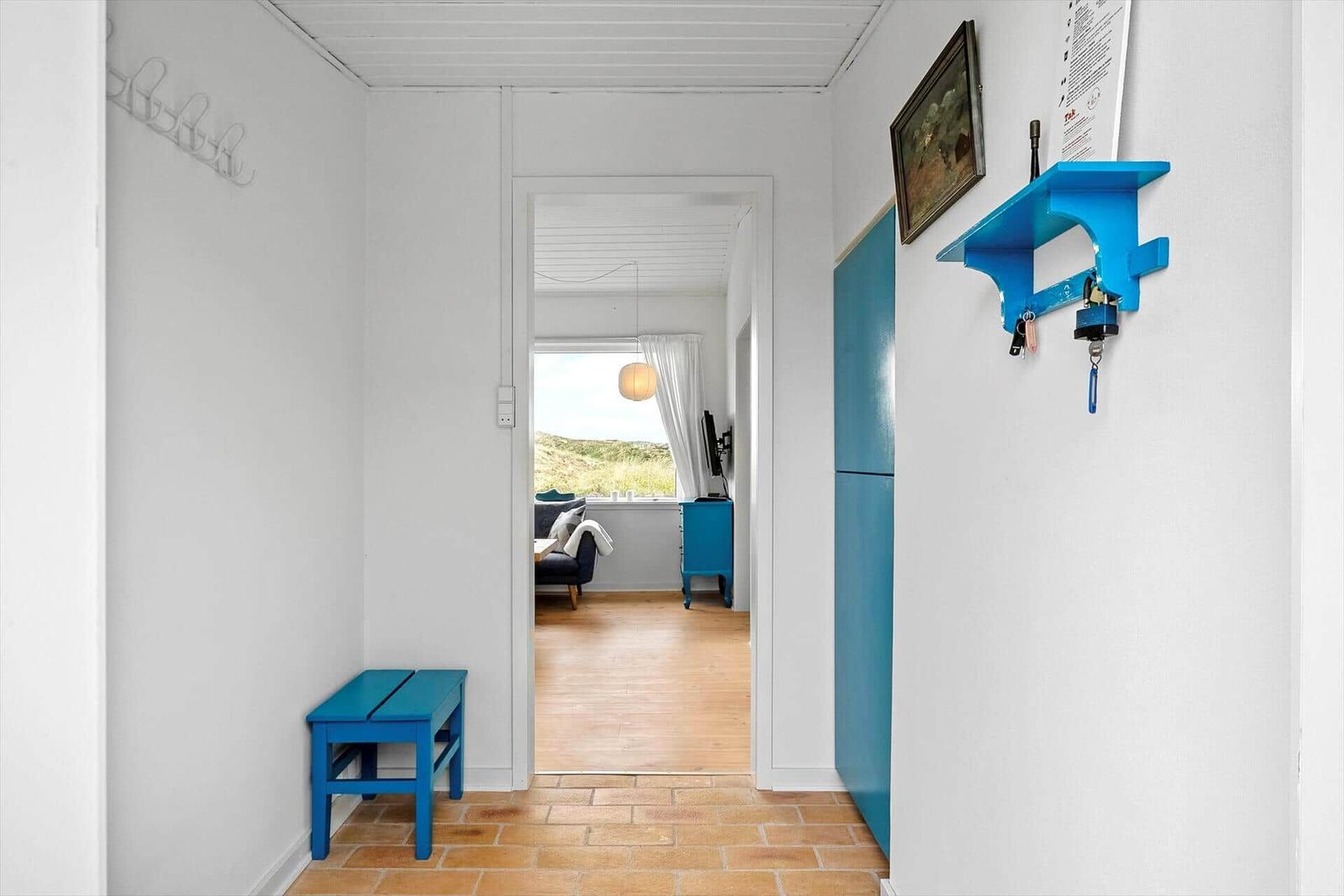 Flur mit blauem Hocker und Schrank. Durchgang in Wohnzimmer mit Blick auf Dünenschlucht.