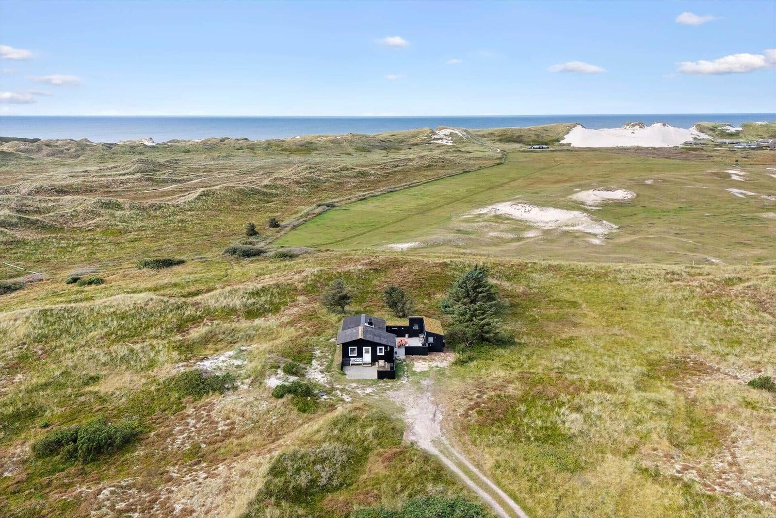 Schwarzes Haus auf grüner Dünenlandschaft mit Blick auf das Meer.