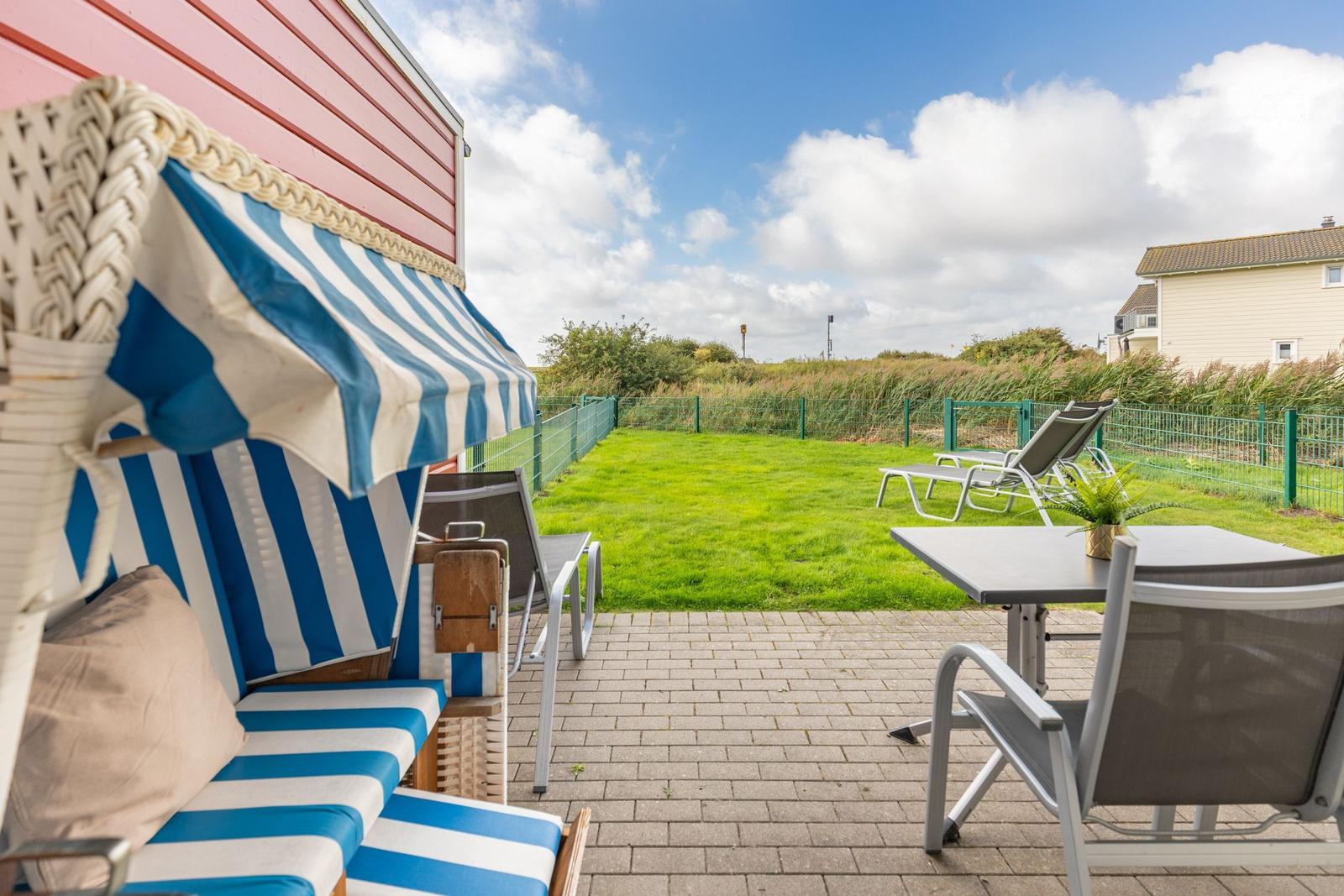 Terrace with loungers, table, and blue-white awning in front of green lawn.