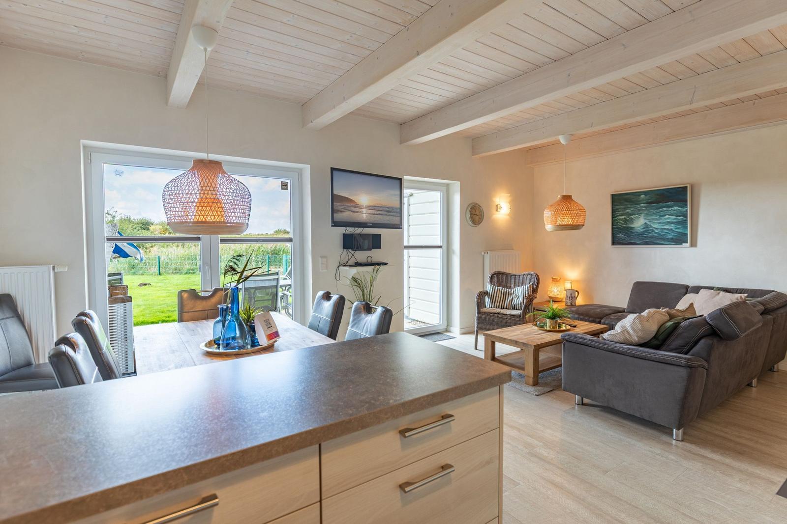 Living and dining area with kitchen island, sofa, and TV. Wooden ceiling and large windows.